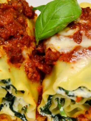 Two servings of rolled lasagna are topped with a thick layer of red sauce, ideal for hearty meals. The pasta is stuffed with a spinach and cheese filling, making it perfect for big gatherings. A fresh basil leaf is placed on top as a garnish.
