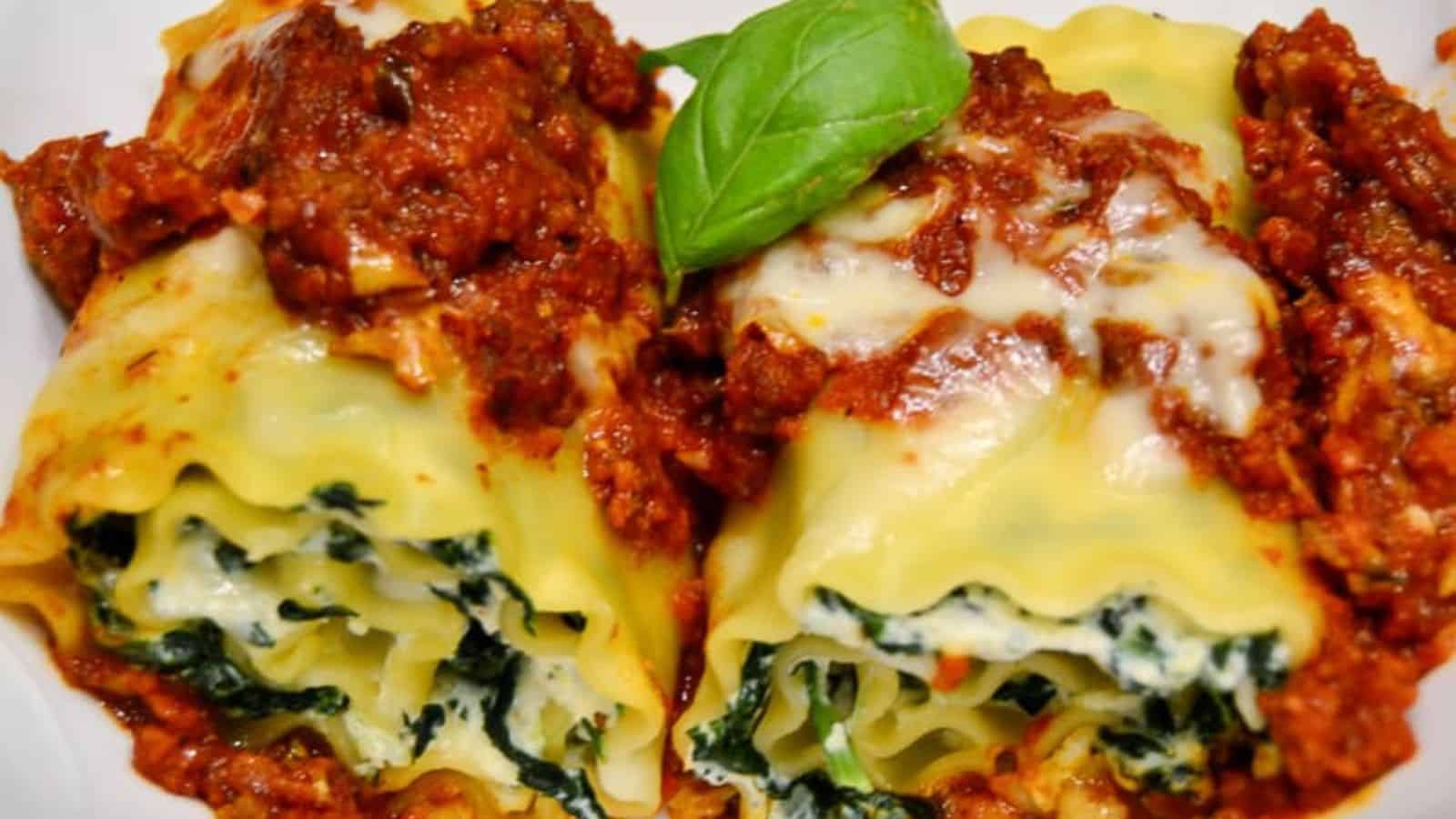 Two servings of rolled lasagna are topped with a thick layer of red sauce, ideal for hearty meals. The pasta is stuffed with a spinach and cheese filling, making it perfect for big gatherings. A fresh basil leaf is placed on top as a garnish.