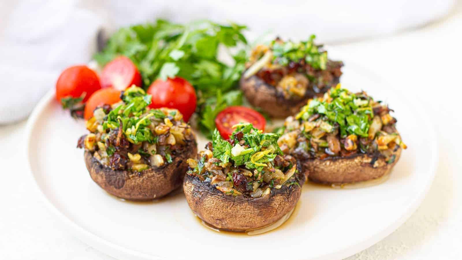 A white plate with vegan stuffed portobello mushrooms garnished with cherry tomatoes and parsley.