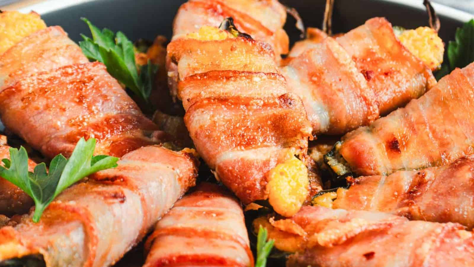 Close-up of bacon-wrapped jalape&ntilde;o poppers in a pan, garnished with parsley leaves. The poppers are crispy and golden brown, with cheese oozing out from the ends.