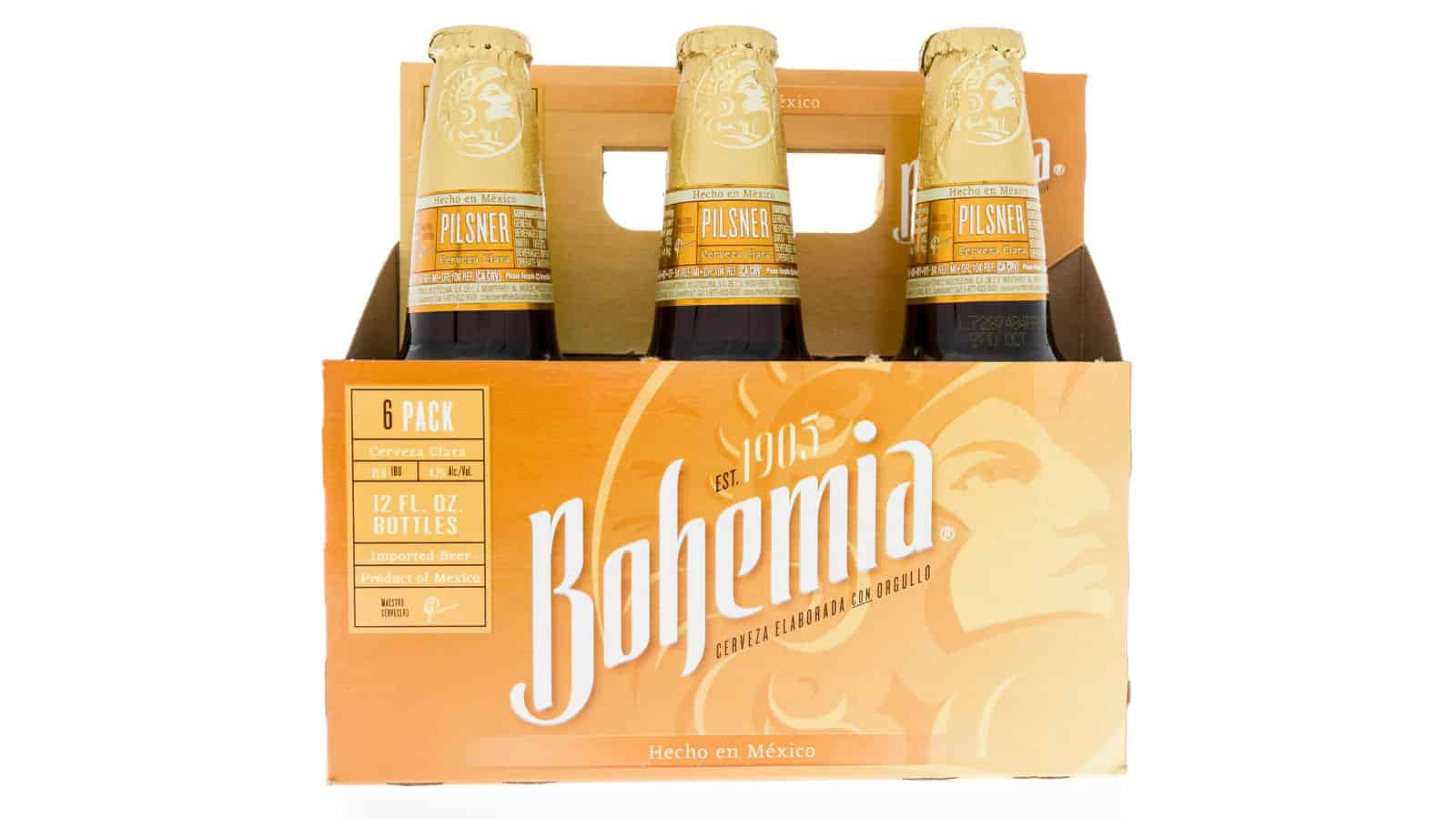 A six-pack of Bohemia Pilsner beer bottles is displayed. The packaging is predominantly orange with white text. The label indicates the brewery's establishment in 1905 and notes that the product is made in Mexico. Each bottle is 12 fluid ounces.