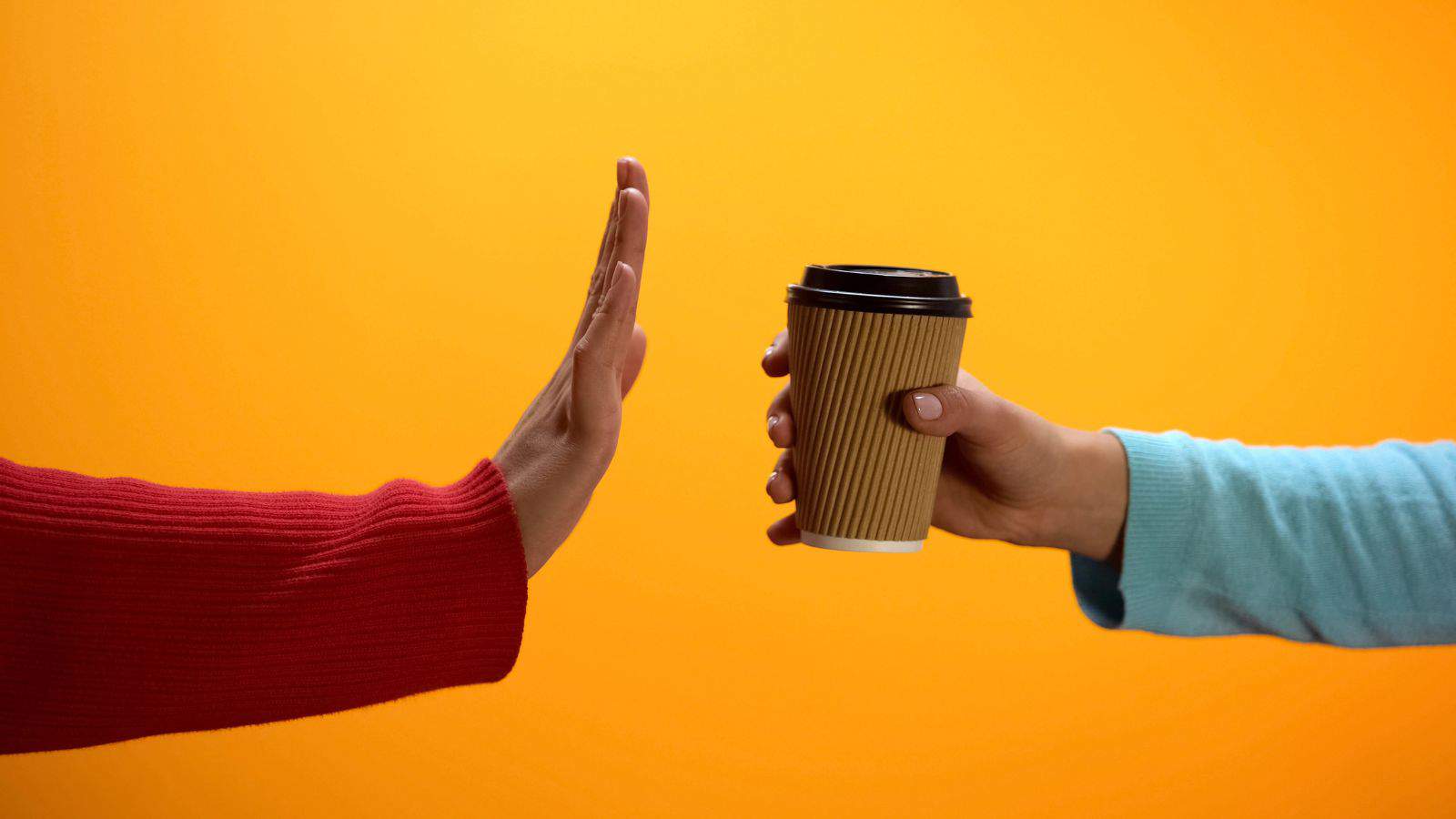 One person wearing a red sweater is gesturing with their hand in a stop motion towards another person in a blue sweater who is holding out a disposable coffee cup. The background is a solid orange color.