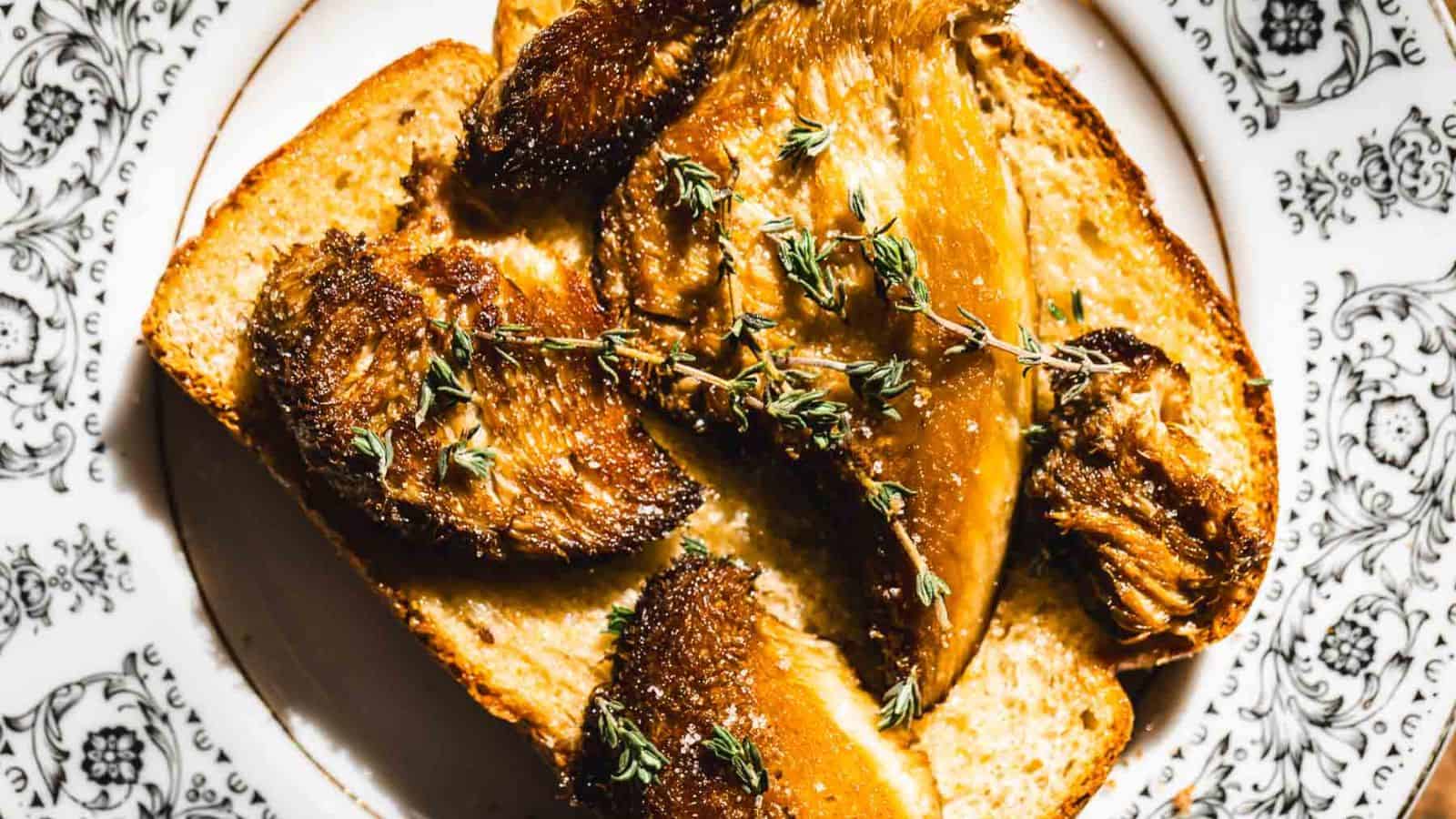 A slice of toasted bread is topped with roasted mushrooms and garnished with sprigs of thyme. The dish is presented on a white plate with black floral patterns.