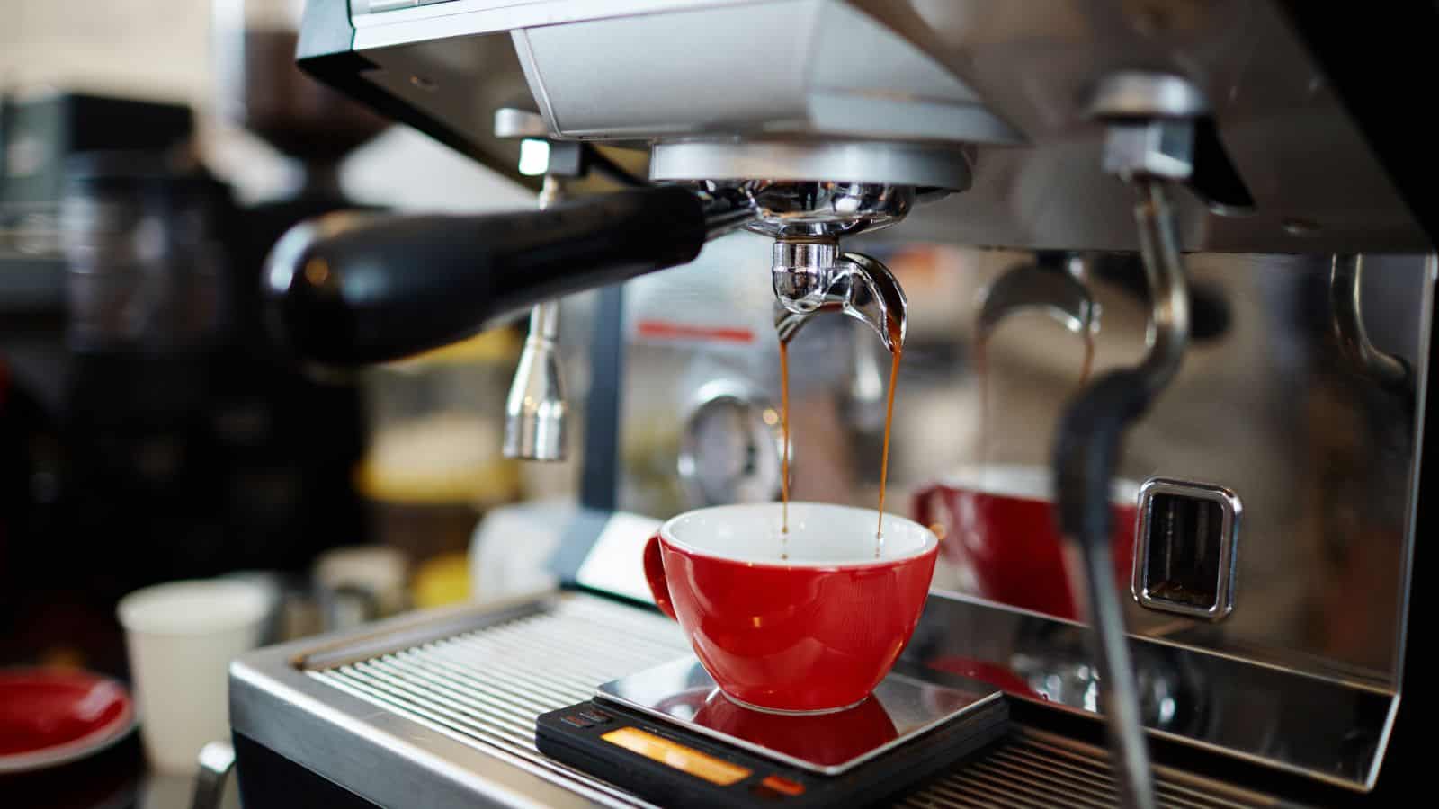 A close-up of an espresso machine brewing coffee into a red cup placed on a scale.