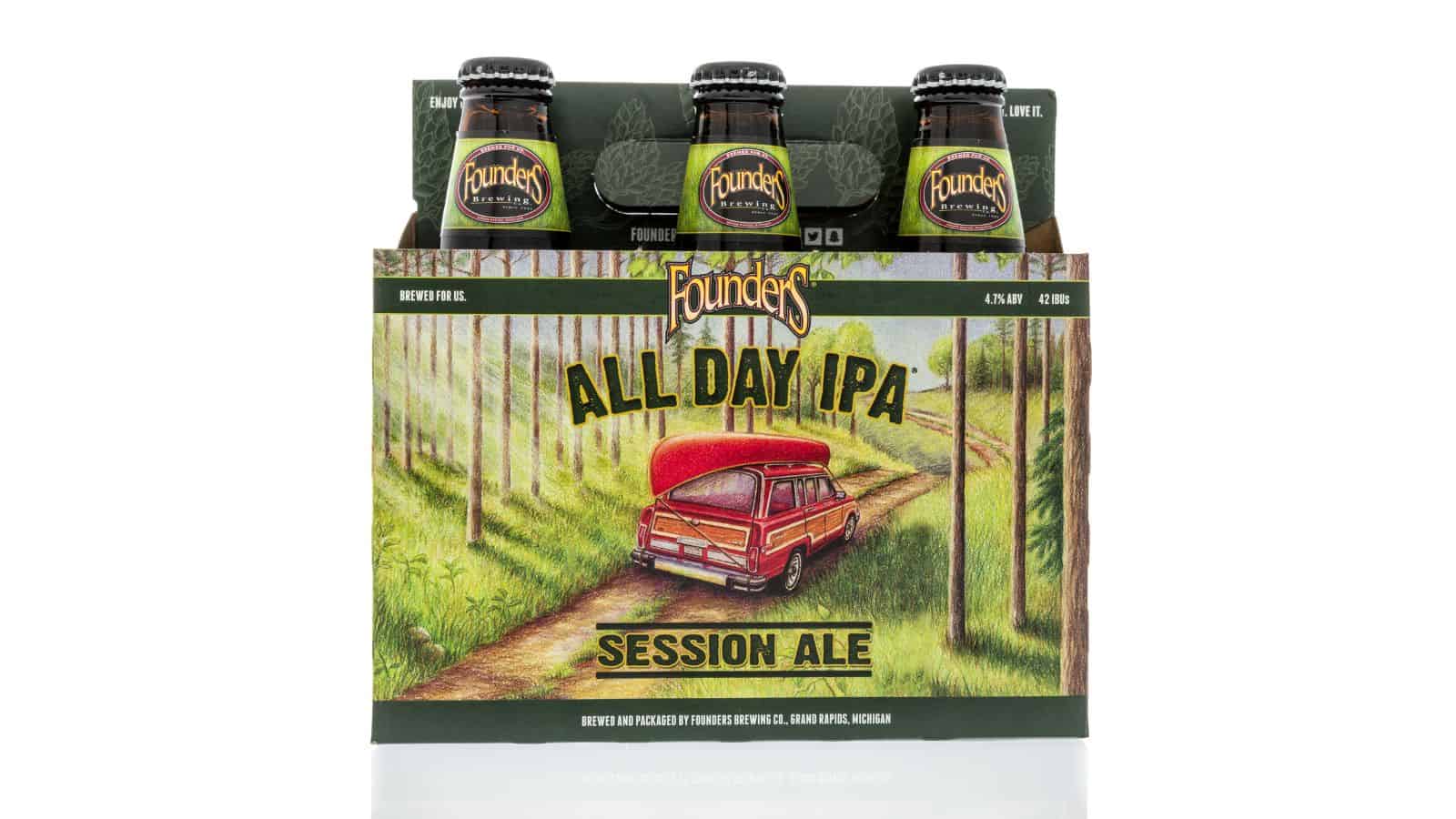 A cardboard holder for Founders All Day IPA Session Ale, featuring four bottles. The packaging is decorated with an illustration of a red car with a canoe on top, driving through a wooded path. The text highlights its brewing location in Grand Rapids, Michigan.