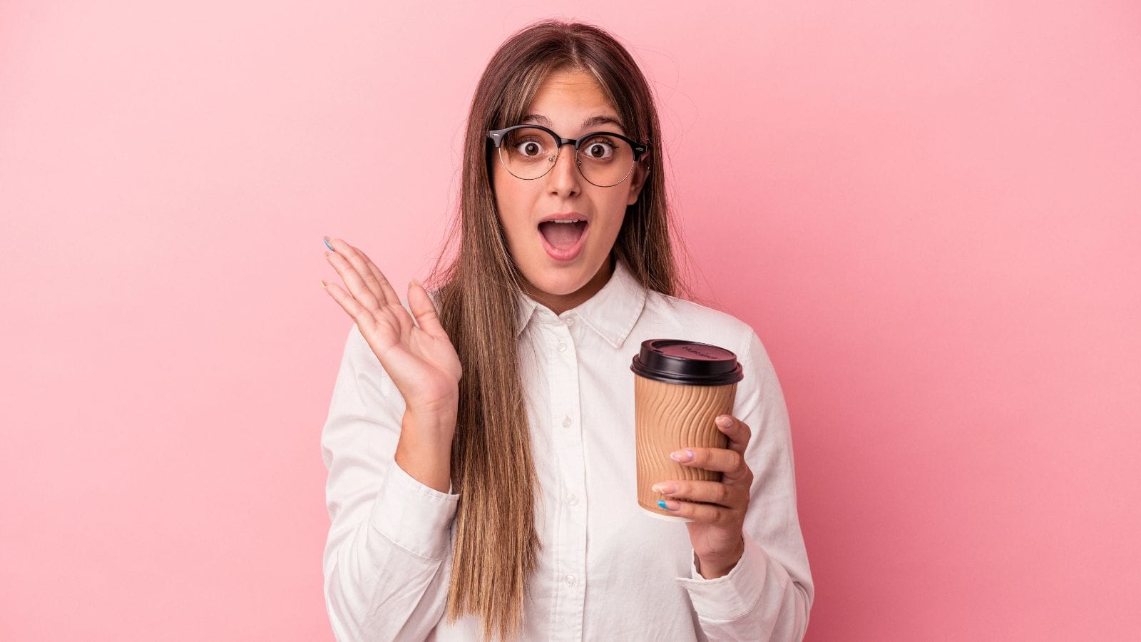 A surprised person with long brown hair and glasses is holding a paper coffee cup. They are wearing a white button-up shirt and standing against a pink background, with their mouth open and one hand raised.