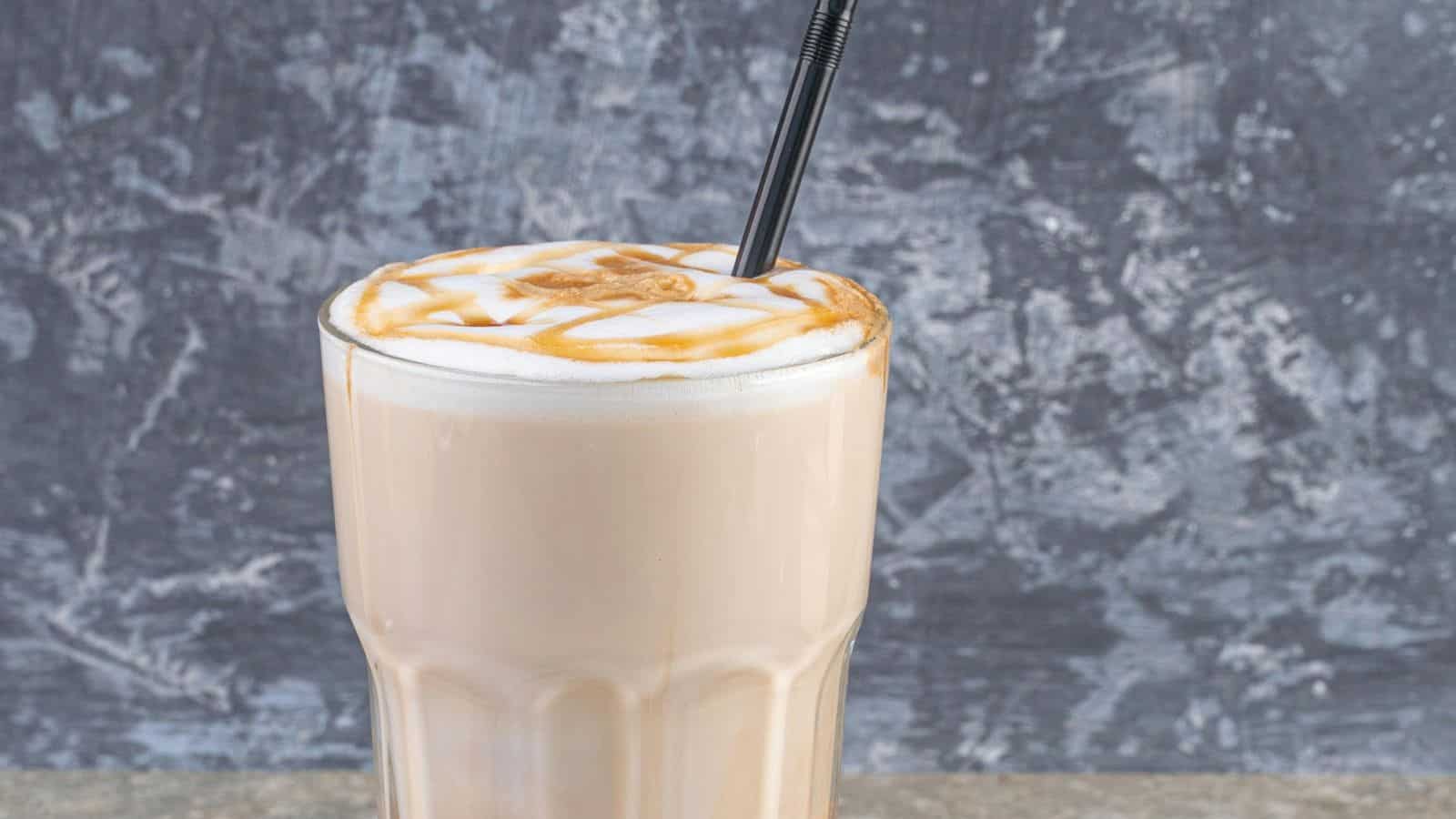 A tall glass of iced coffee with silky cold foam and caramel drizzle on top, featuring a black straw. Set against a textured gray background, it invites you to achieve that perfect coffee shop experience at home.