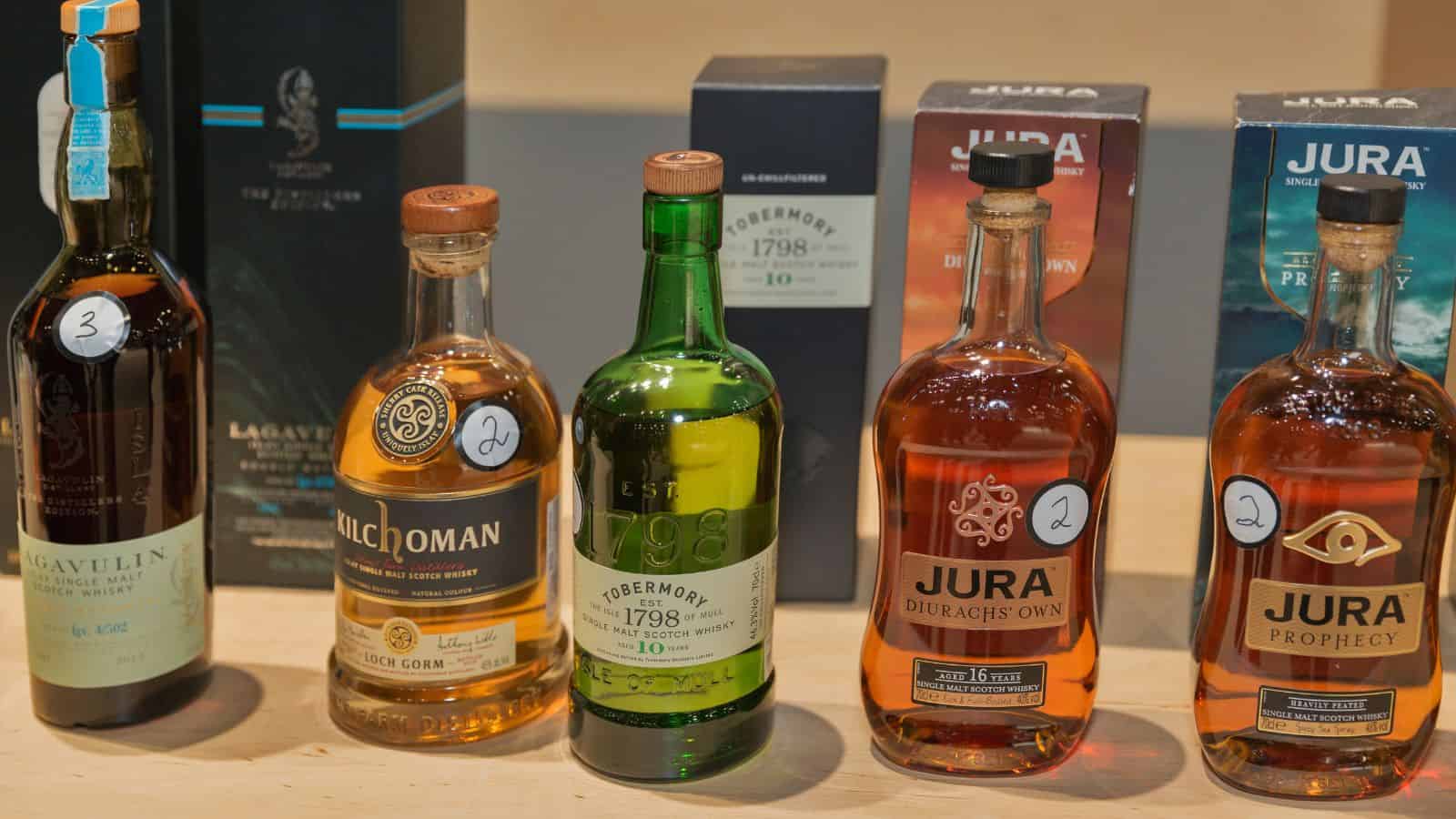 A selection of six whiskey bottles displayed in a row. The bottles have various shapes, labels, and colors, with numbers from 1 to 6 on them. Their packaging boxes are visible in the background.