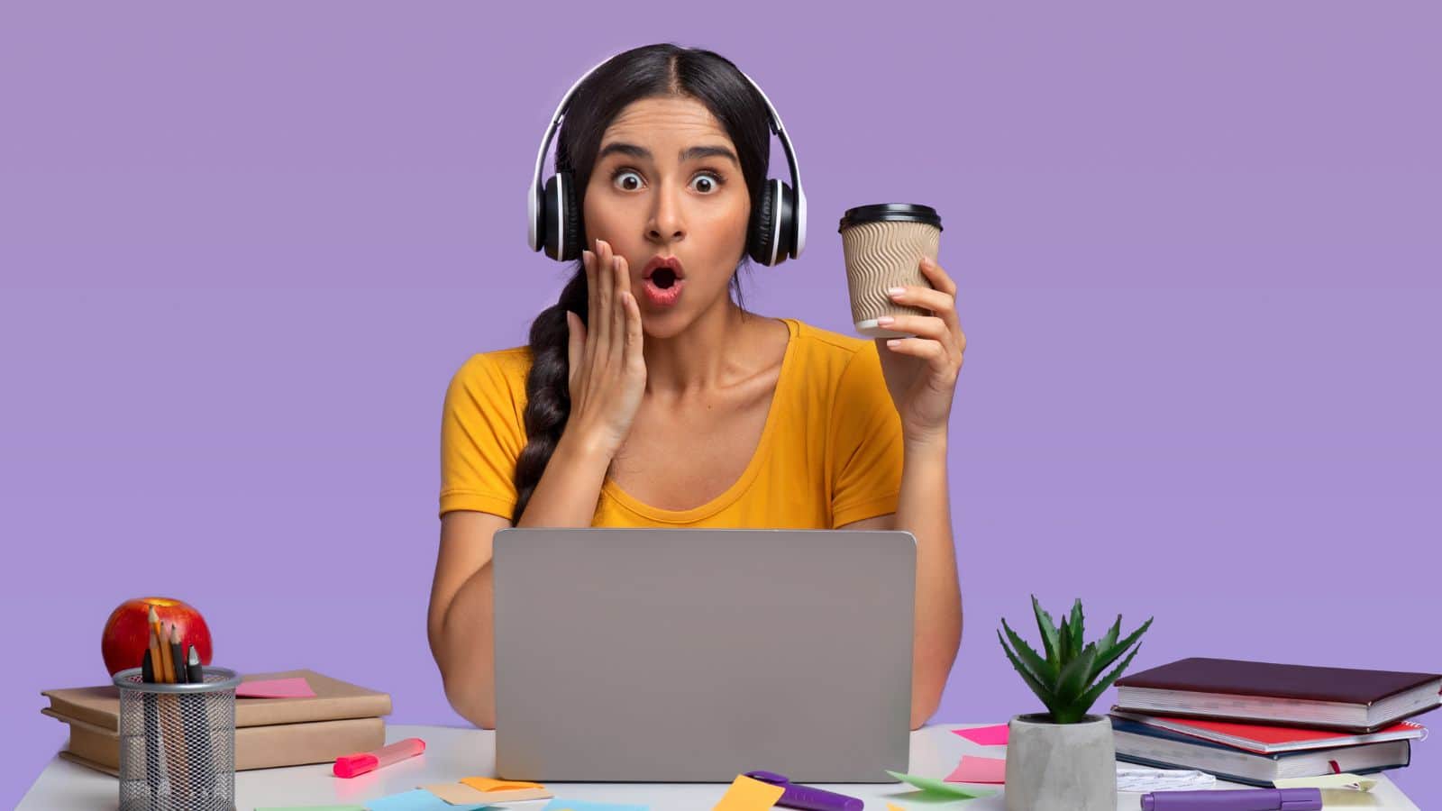 A woman in a yellow shirt sits at a desk with a laptop. She wears headphones and holds a coffee cup, looking surprised. The desk has books, notepads, an apple, sticky notes, a plant, and a pen holder. The background is purple.