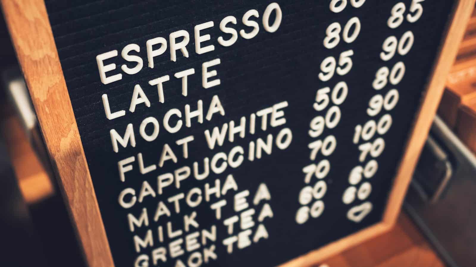 A menu board displaying drink options and prices: Espresso 80, Latte 90, Mocha 90, Flat White 90, Cappuccino 70, Matcha 60, Milk Tea 60, Green Tea 60, and Black Tea 60.