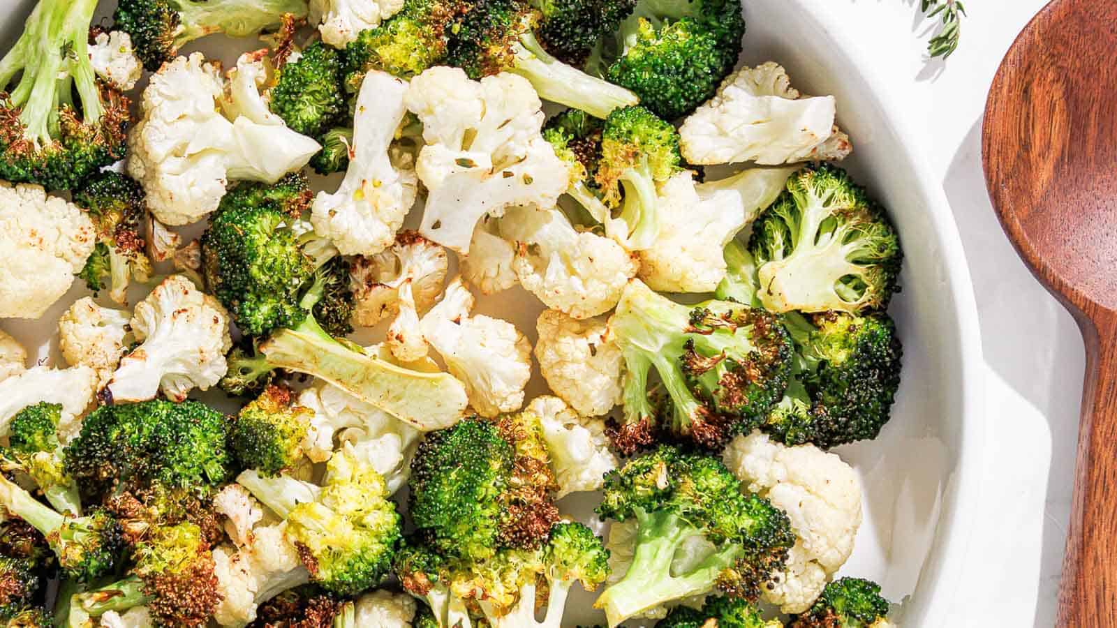 air fryer broccoli and cauliflower on a white plate with a pink linen and thyme.