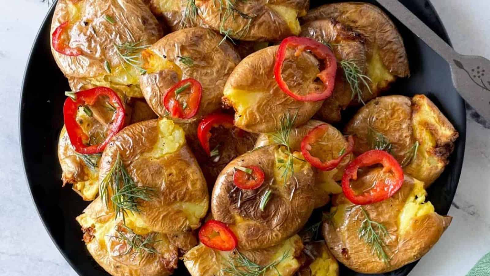 Closeup of crispy smashed potatoes with dill and chili slices.
