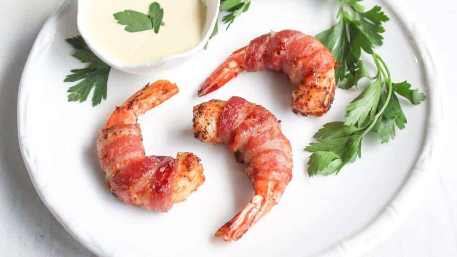 Bacon wrapped shrimp on a white plate with dipping sauce.