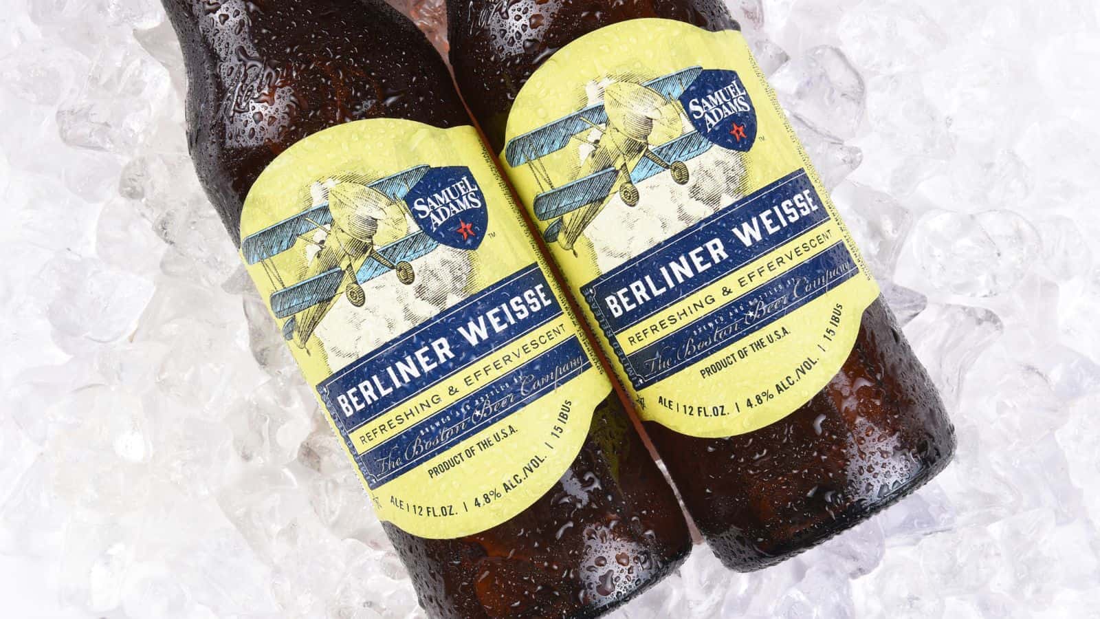 Two bottles of Berliner Weisse beer are lying on ice. Each bottle has a yellow label featuring a vintage airplane and blue text. The labels also read "Refreshing & Effervescent" and show a volume of 12 FL OZ and alcohol content of 4.8% ALC/Vol.