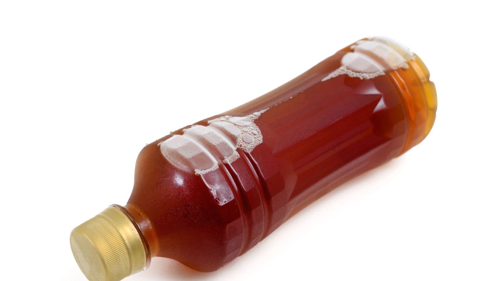 A plastic bottle filled with a brown liquid, lying on its side against a white background. The bottle has a gold-colored screw cap and visible bubbles inside the liquid near the top.