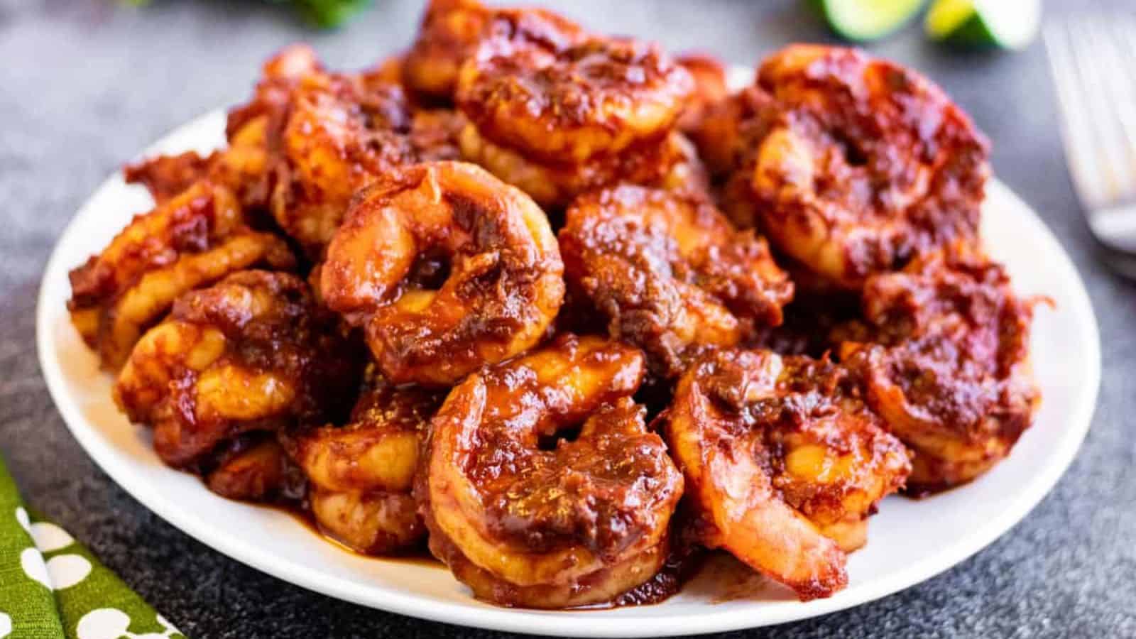 Shrimp in red chile sauce on a white plate with lime wedges and a fork in the background.