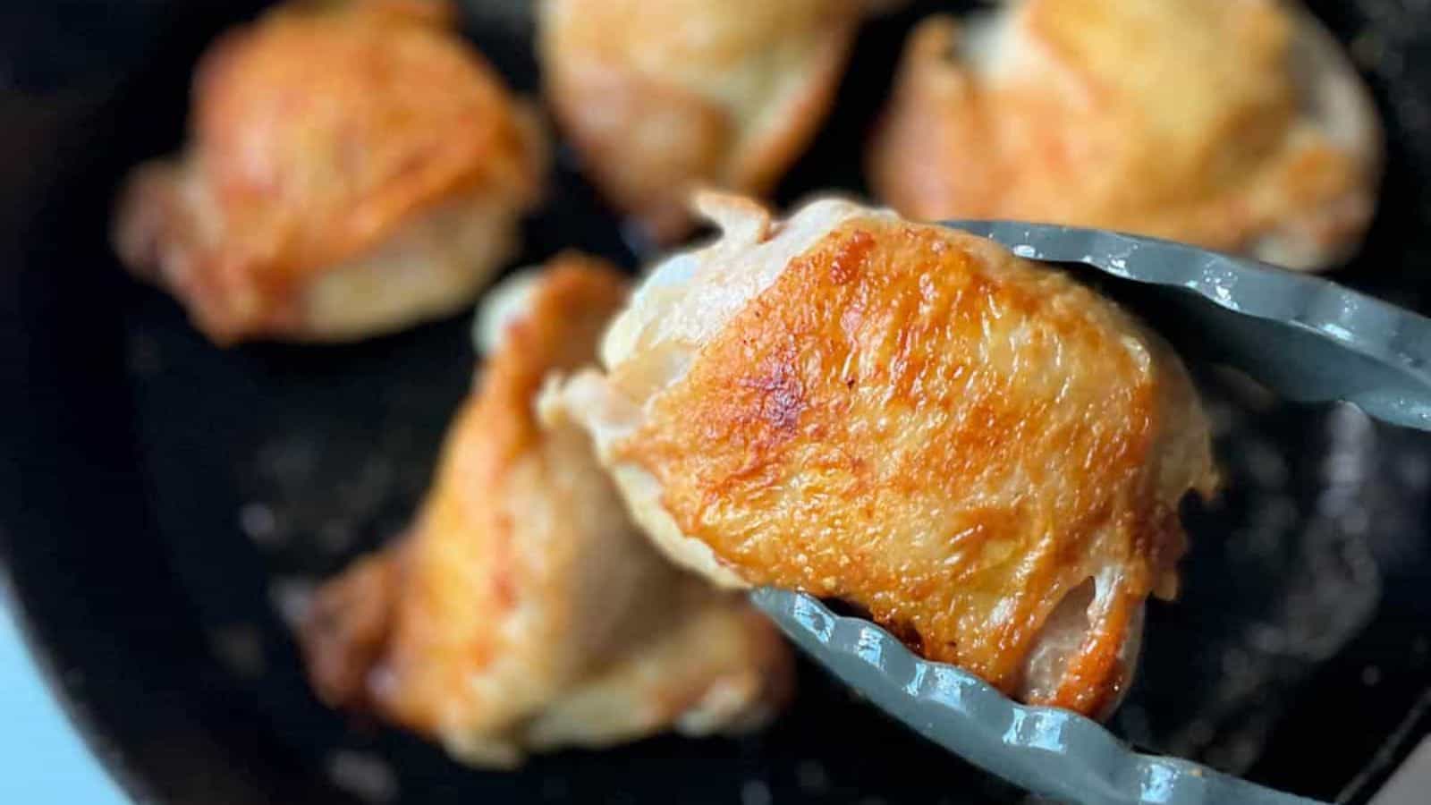 Closeup overhead shot of 3 crispy chicken thighs in a black cast iron skillet.