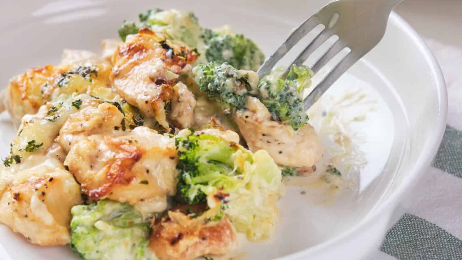 A wooden spoon scooping chicken broccoli alfredo casserole out of a serving dish.