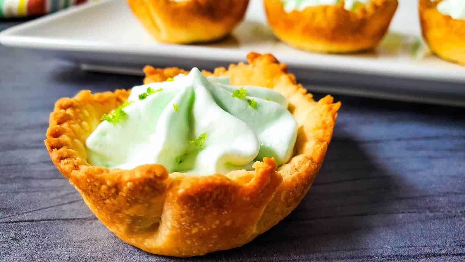 A front view of a mini key lime pie with more on a white plate in the background.