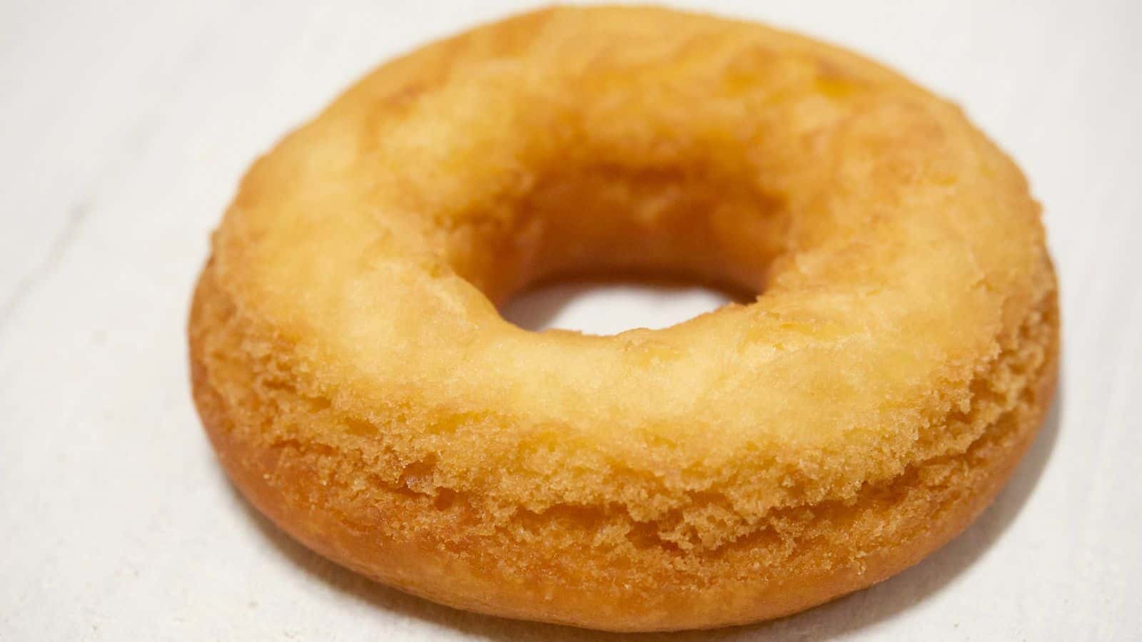A plain, golden-brown cake doughnut with a slightly rough texture, placed on a light surface.