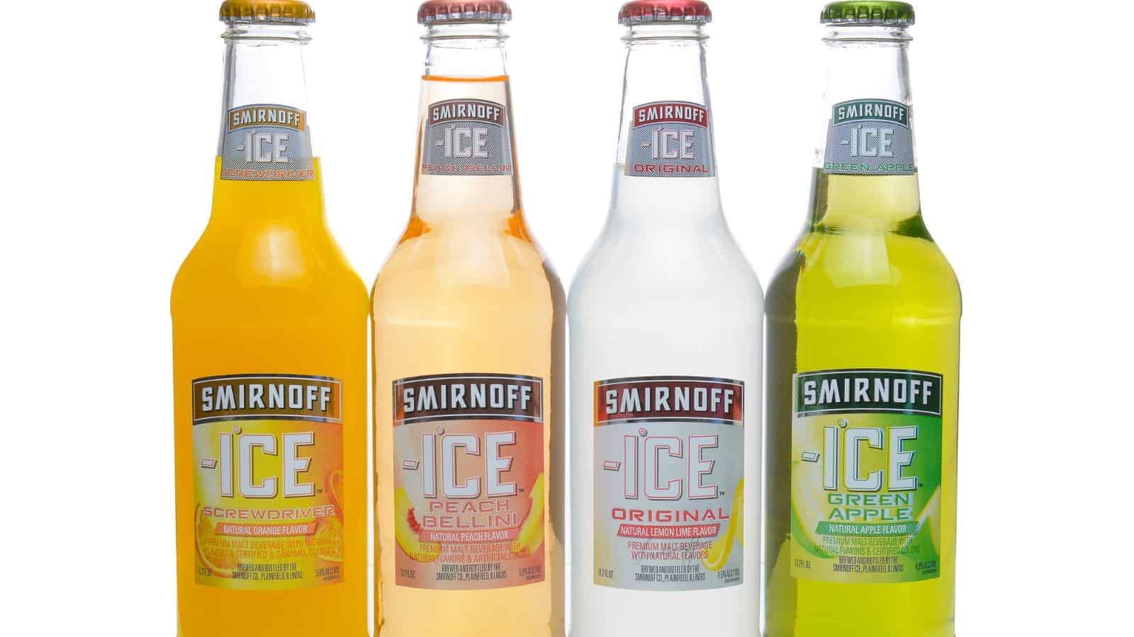 Four bottles of Smirnoff Ice are shown in a row. The flavors from left to right are Screwdriver, Peach Bellini, Original, and Green Apple. The bottles are clear with colored liquid inside and silver caps.