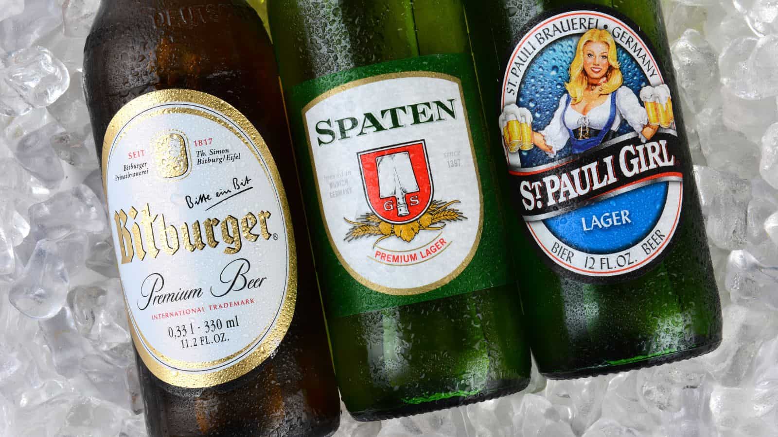 Three beer bottles are placed on ice. The brands visible are Bitburger Premium Beer, Spaten Premium Lager, and St. Pauli Girl Lager. The bottles are partially covered with ice, and condensation is visible on their surfaces.