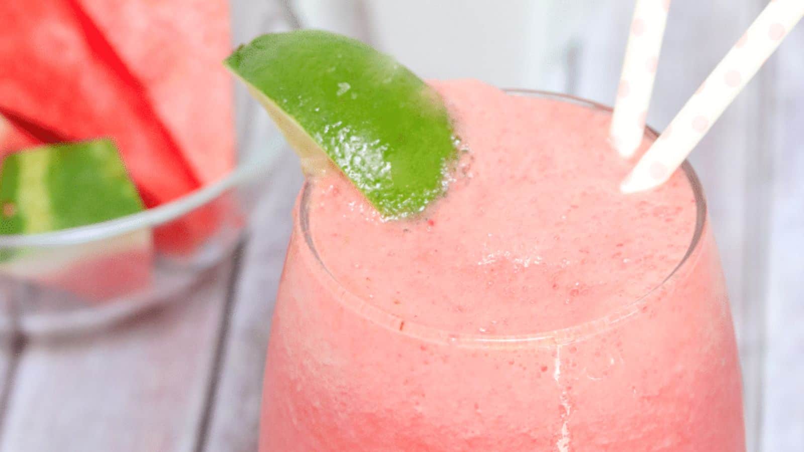 Pink watermelon slushie in a glass garnished with lime and more watermelon and lime behind it.