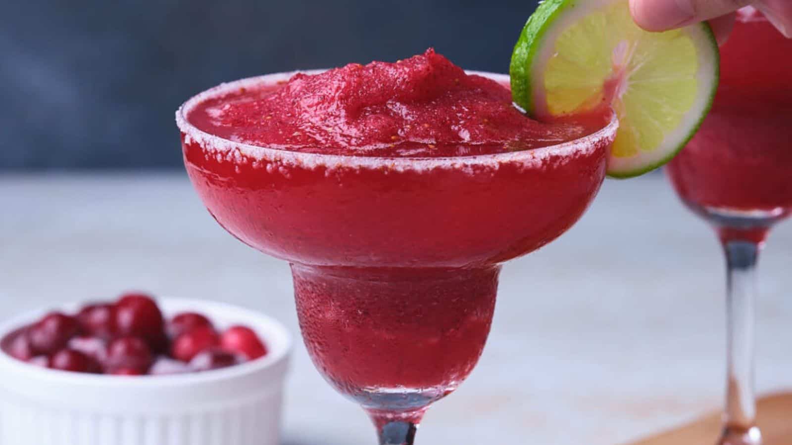 Two red frozen cranberry margaritas garnished with lime slices.