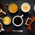 Top view of various coffee drinks, coffee beans, ground coffee, and a milk jug on a dark surface-a perfect guide to different types of coffee.