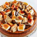 A pumpkin smores cheesecake topped with toasted marshmallows, rich chocolate pieces, and graham cracker chunks.