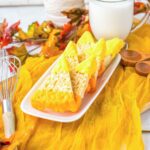Candy corn Rice Krispies treats dipped in yellow and orange chocolate, arranged on a white plate with a glass of milk.
