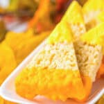 Candy corn Rice Krispies treats shaped like classic candy, dipped in yellow and orange icing, arranged on a white plate.
