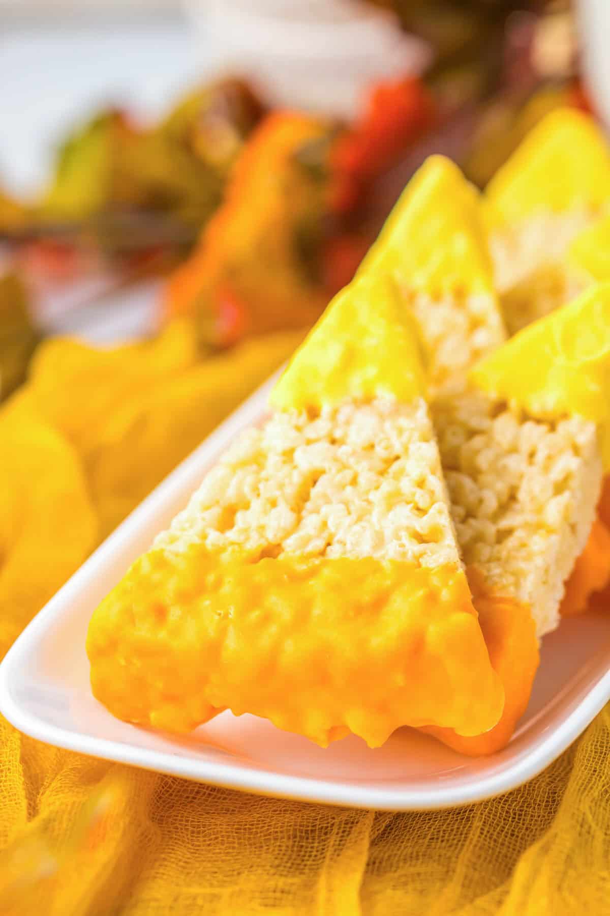 Candy corn Rice Krispies treats shaped like classic candy, dipped in yellow and orange icing, arranged on a white plate.