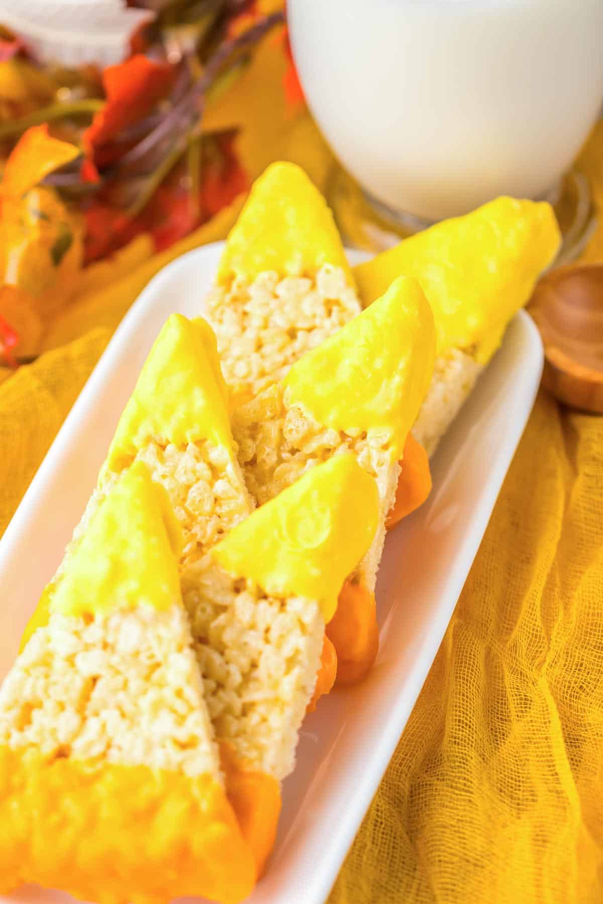 Triangle-shaped Candy Corn Rice Krispies treats dipped in yellow and orange candy melts, perfectly resembling classic candy corn.