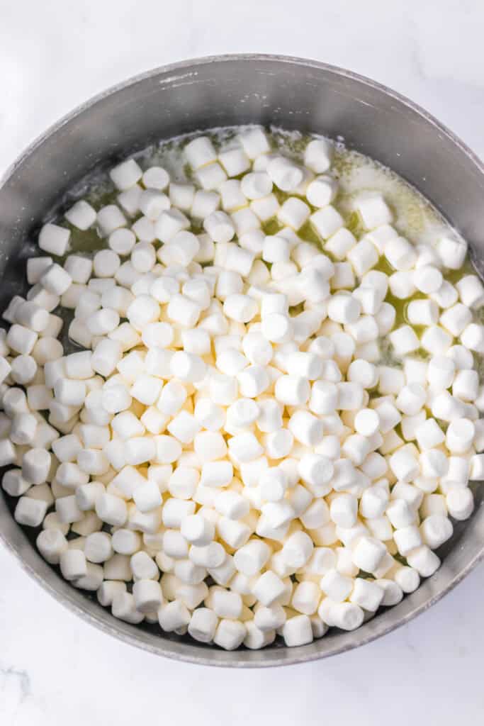 A pot filled with mini marshmallows and melted butter, ready to be mixed for delicious candy corn Rice Krispies treats.
