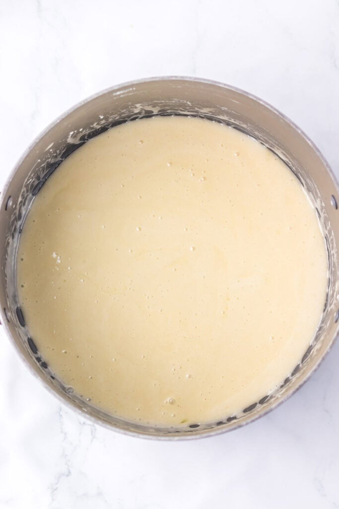 A mixing bowl filled with smooth, pale yellow batter for candy corn rice krispies rests on a white surface.