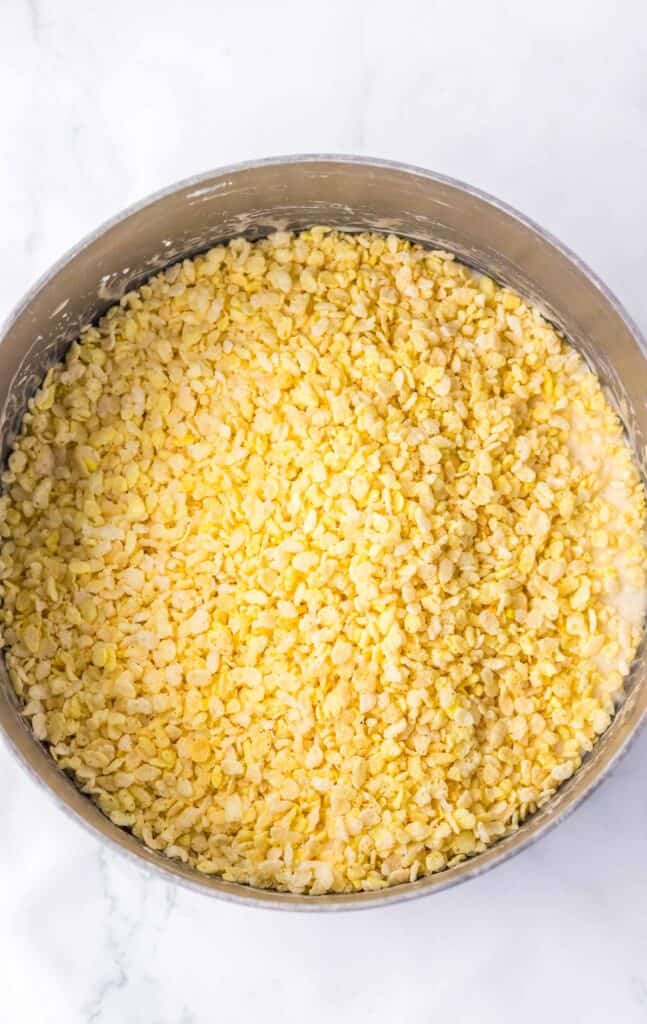 A bowl filled with candy corn Rice Krispies cereal mixed with melted marshmallows on a white marble surface.