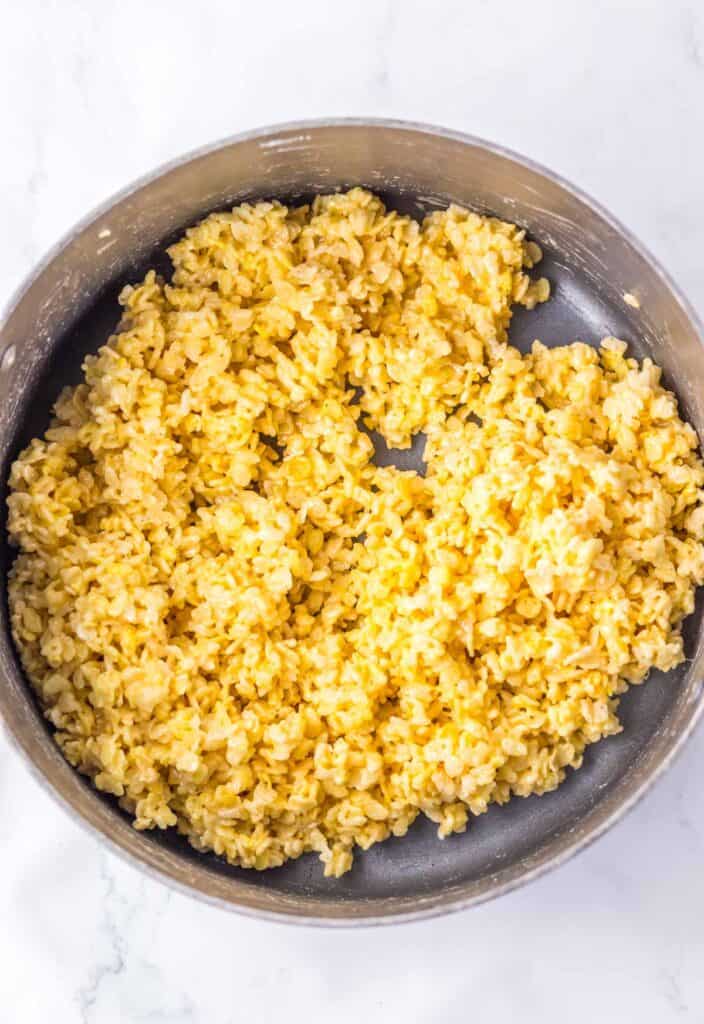 A pan filled with cooked, yellow-tinted rice on a white marble surface, reminiscent of the cheerful hues in candy corn rice krispies.