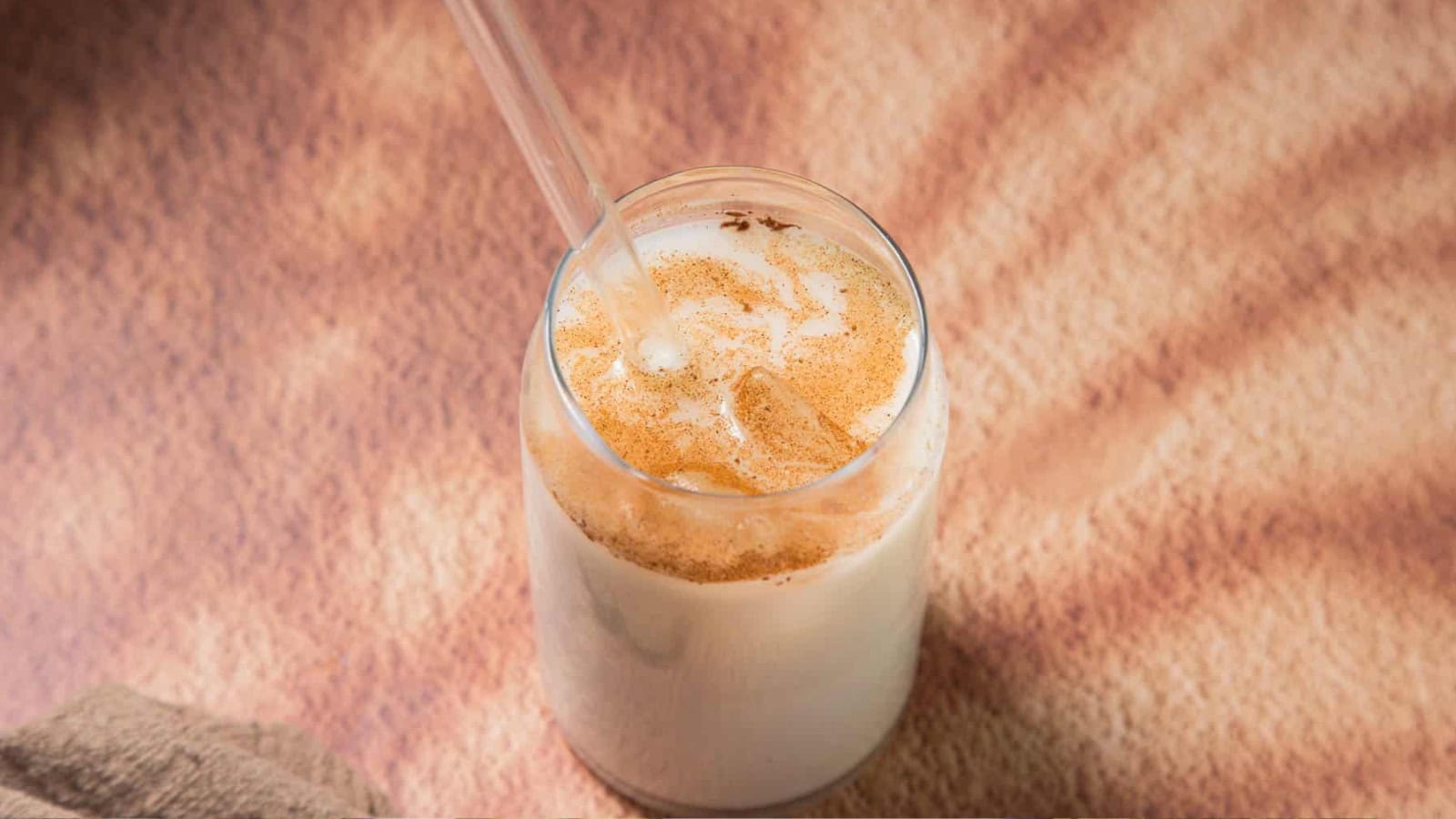 A glass of iced horchata topped with cinnamon, with a straw, on a sunlit surface.