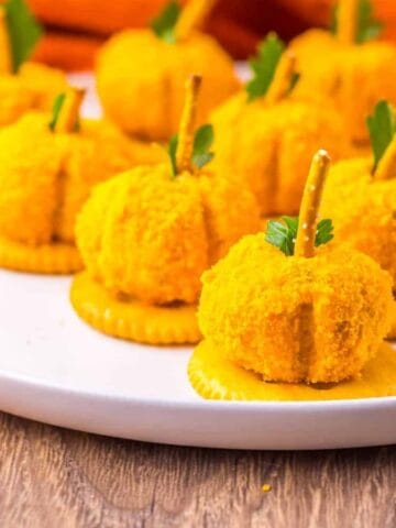 Mini pumpkin-shaped cheese balls on crackers with pretzel stems.
