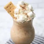 S'mores milkshake topped with whipped cream, mini marshmallows, cocoa powder, and a graham cracker for a classic campfire-inspired treat.