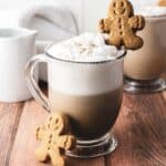 A mug of frothy coffee topped with a gingerbread cookie, with another cookie leaning against the mug&mdash;the perfect cozy latte moment inspired by a homemade Gingerbread Latte recipe.