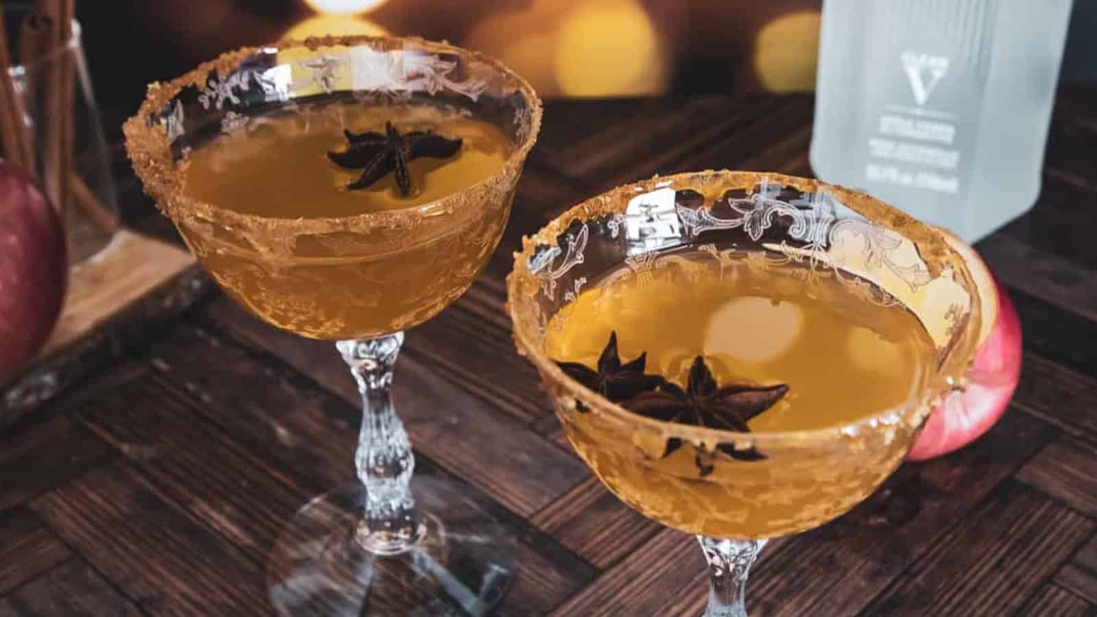 Two elegant cocktail glasses filled with amber liquid, garnished with star anise, on a wooden table.