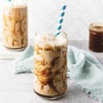 A glass of iced caramel coffee with caramel drizzle and a striped straw sits on a light surface with a blue cloth.