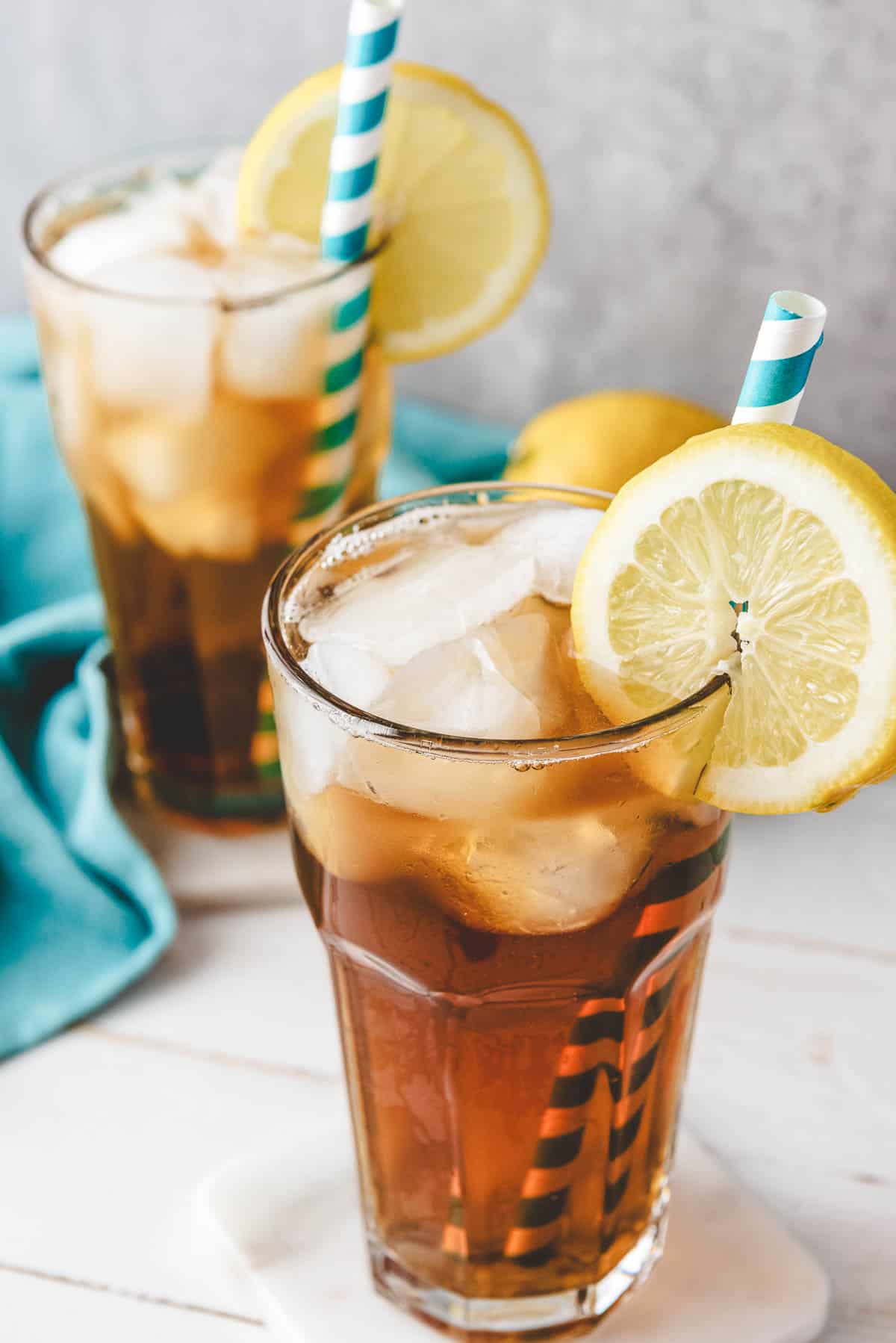 Two glasses of homemade sweet tea with lemon slices and striped straws sit on a white surface.