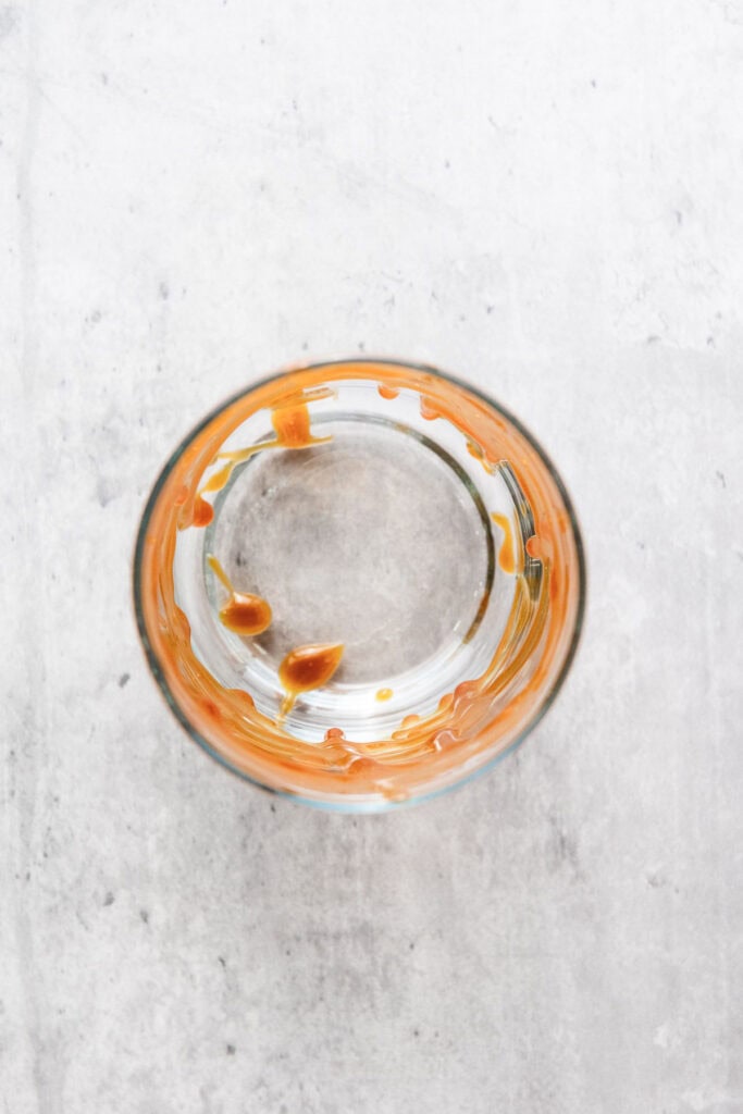 A glass with remnants of orange liquid around the rim, viewed from above on a light surface, hints at a recently finished iced caramel coffee.