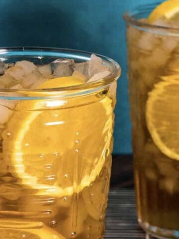 Two glasses of iced tea with lemon slices and glass straws against a blue background.