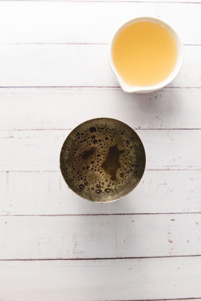 A cup of black coffee and a white cup of tea sit on a white wooden surface, perfect alongside a crisp glass of ginger beer.