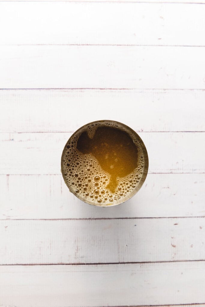 A cup of frothy coffee seen from above on a white wooden surface, with hints of apple cider lending a unique twist to the classic brew.