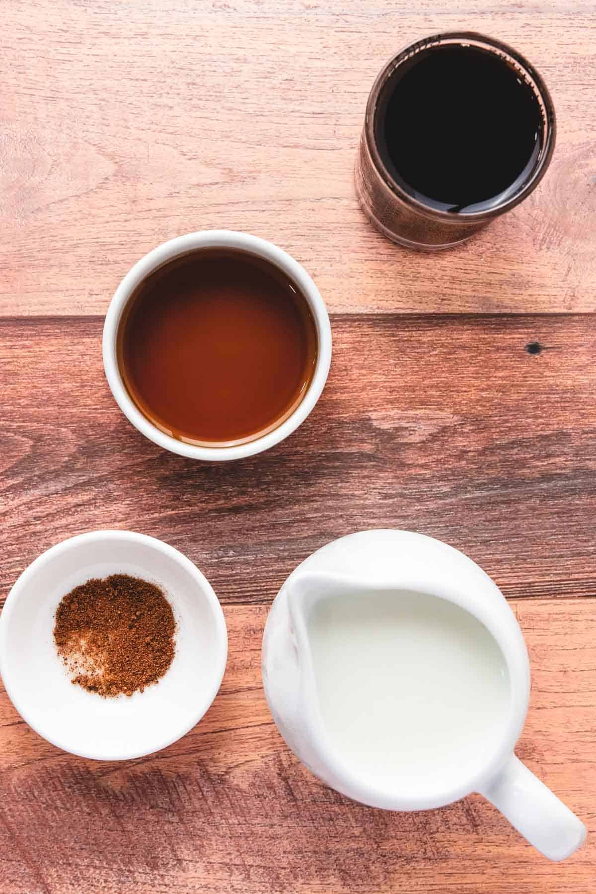 Four containers with coffee, syrup, spices, and milk on a wooden surface, viewed from above&mdash;perfect ingredients for a cozy Gingerbread Latte recipe.